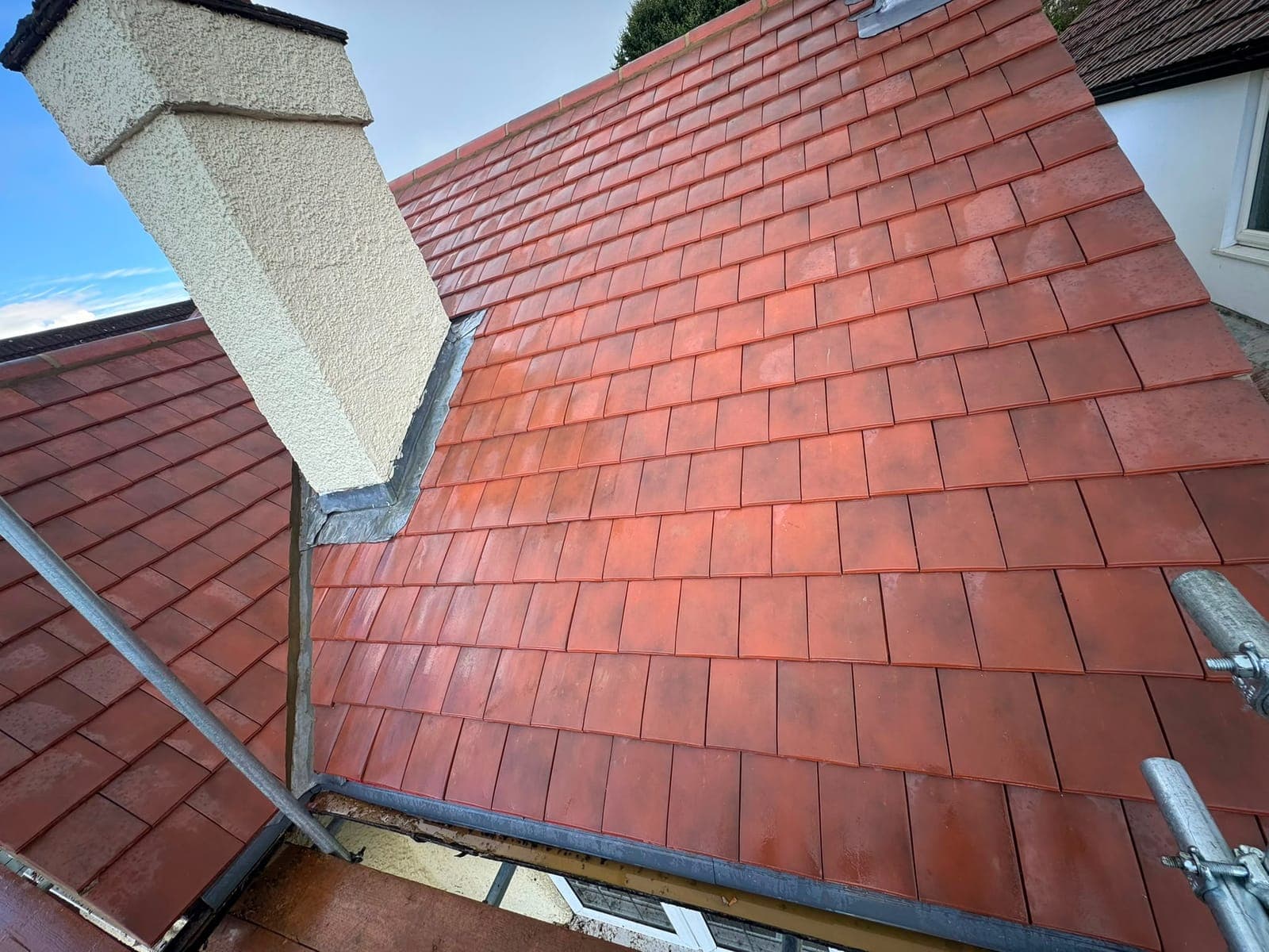 New red clay tile roof with a lead-lined valley and neat lead flashing around a rendered chimney