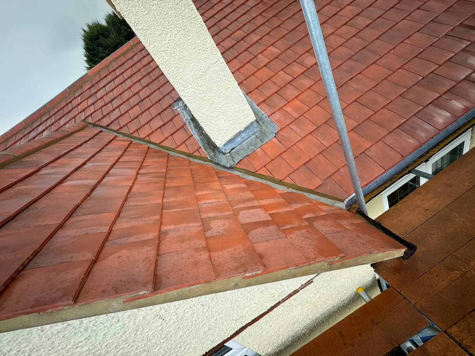 New red clay plain tile roof with lead flashing around a rendered chimney and tiled ridge