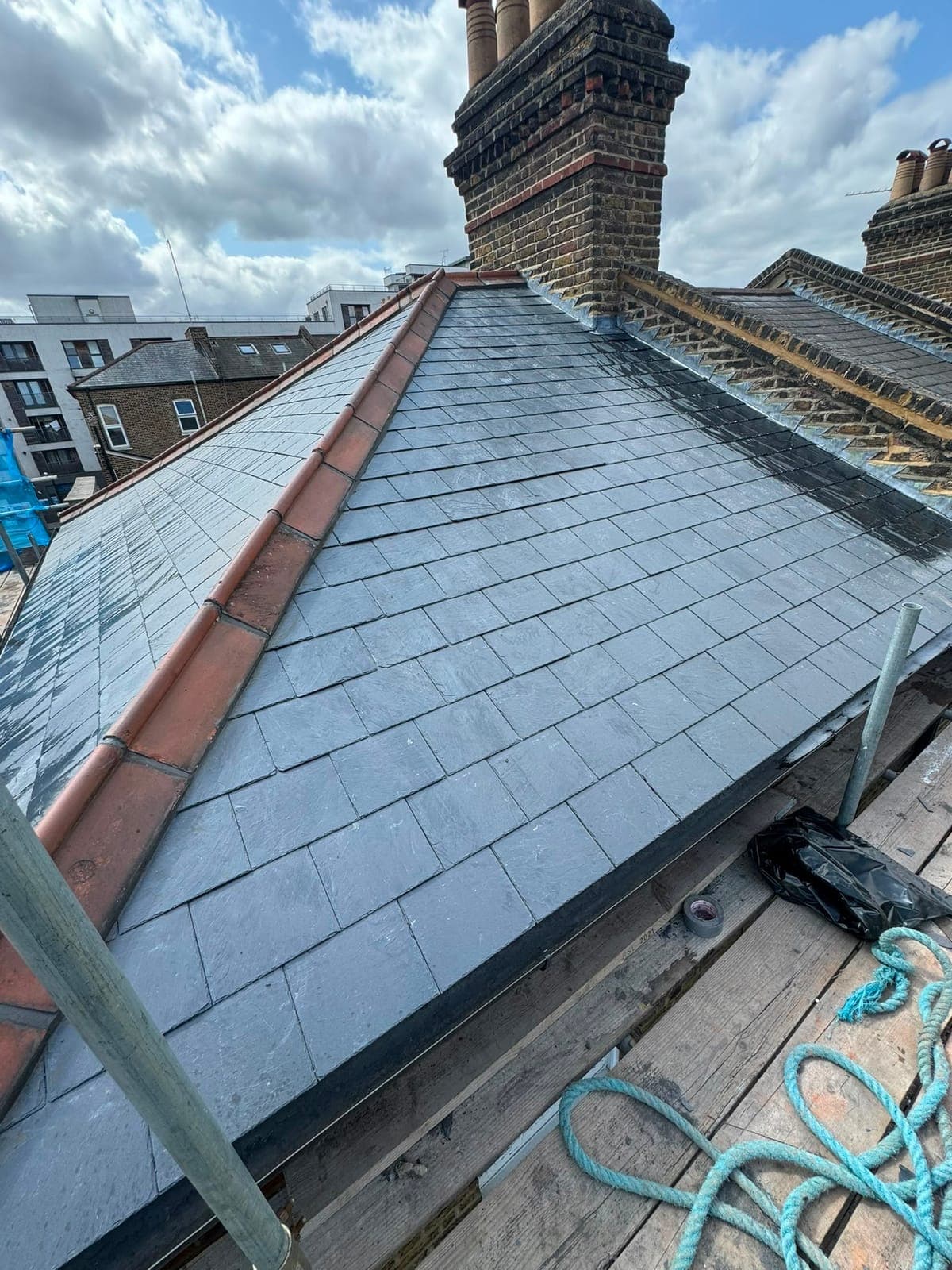 Newly laid slate roof with terracotta ridge and hip tiles beside traditional yellow-brick chimney stacks