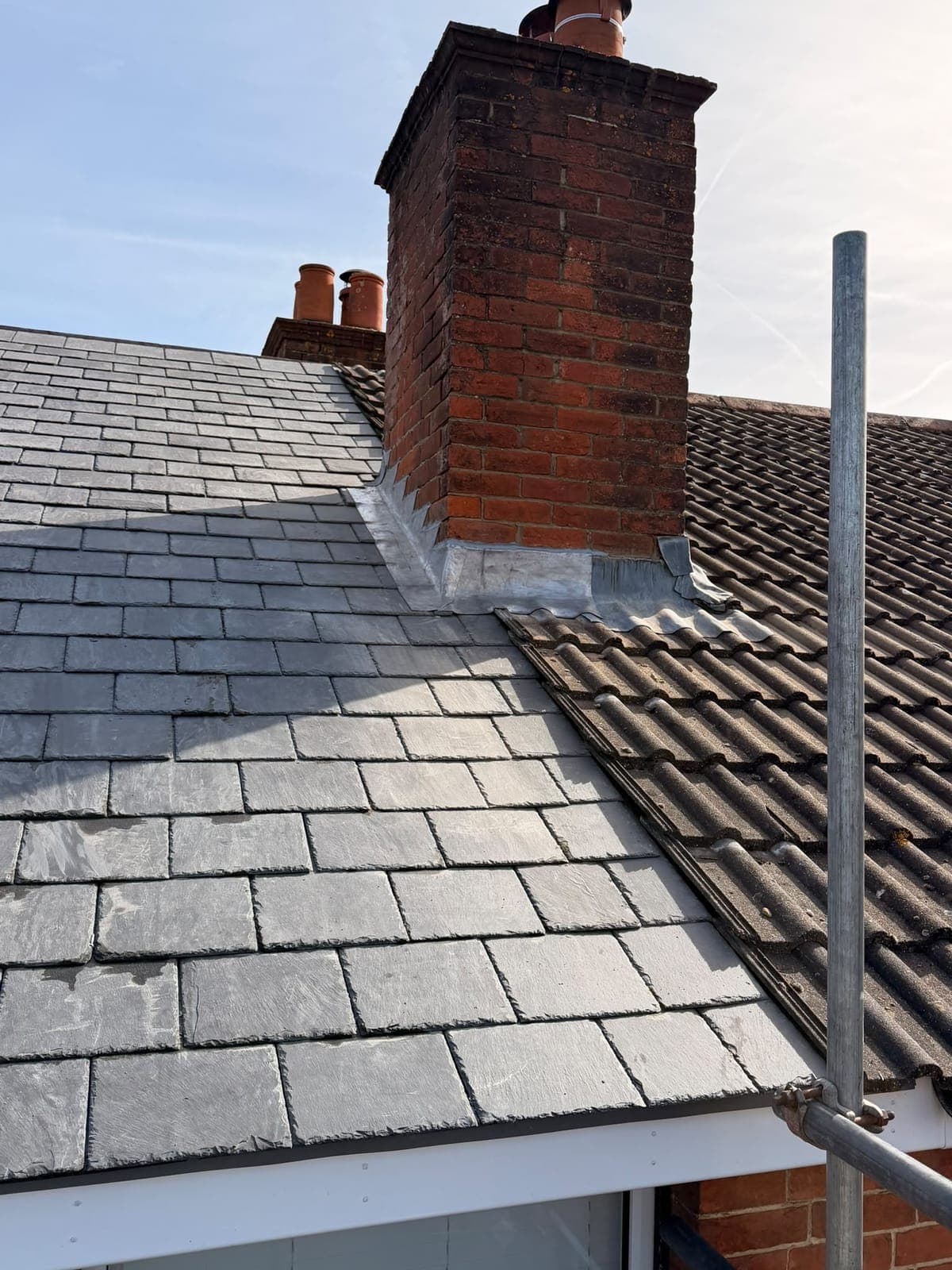 Brick chimney with new lead flashing where a new slate roof meets the older concrete-tiled roof next to it