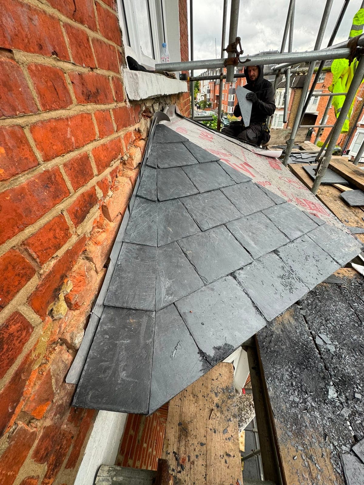 Roofer fitting a cut slate beside the lead flashing on a roof under construction, with breathable membrane still showing