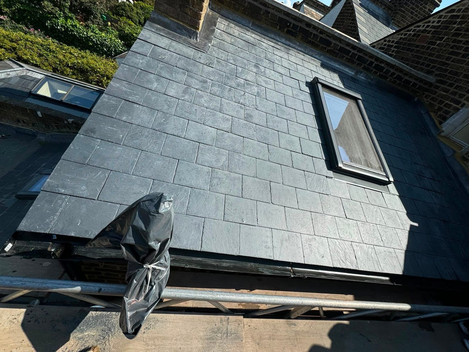 New slate roof with a roof window fitted and lead flashing running along the chimney and party wall